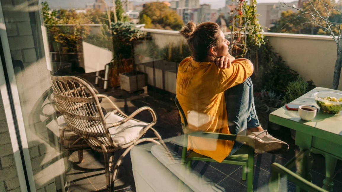 A woman sitting on a chair on a balcony looking out.